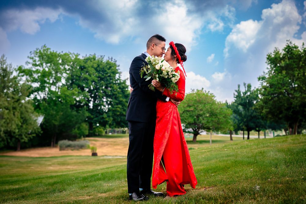 Wedding couple poses in grassy field under dramatic blue sky.