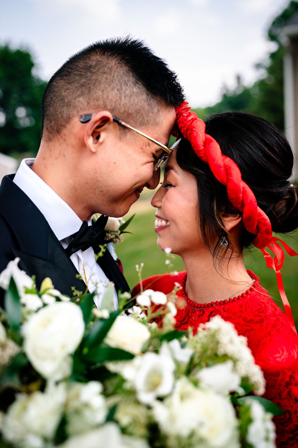 Romantic wedding portrait with white flowers and red accents in outdoor setting.
