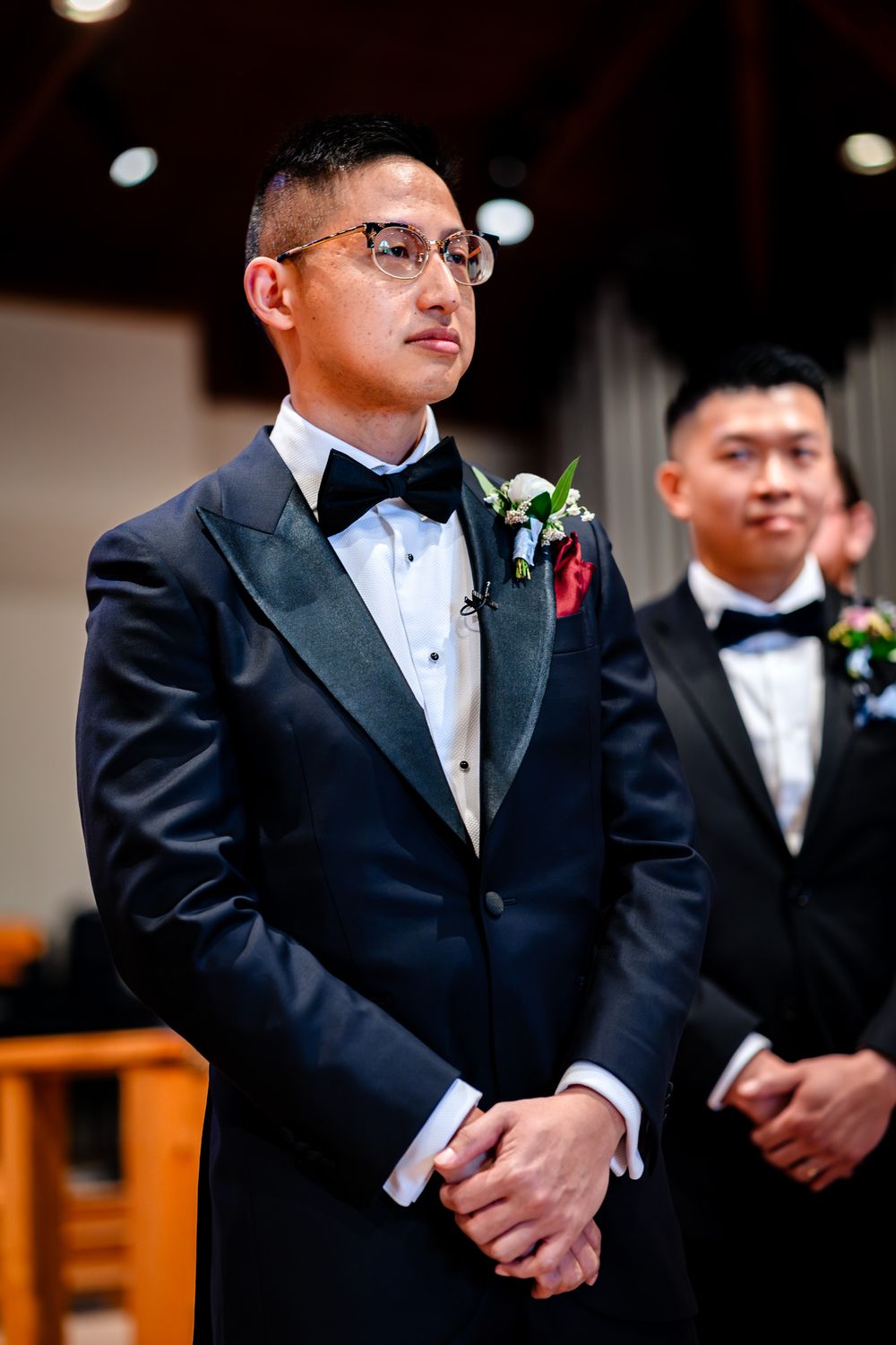 Groomsmen in black tuxedos and bowties stand at attention during wedding ceremony.