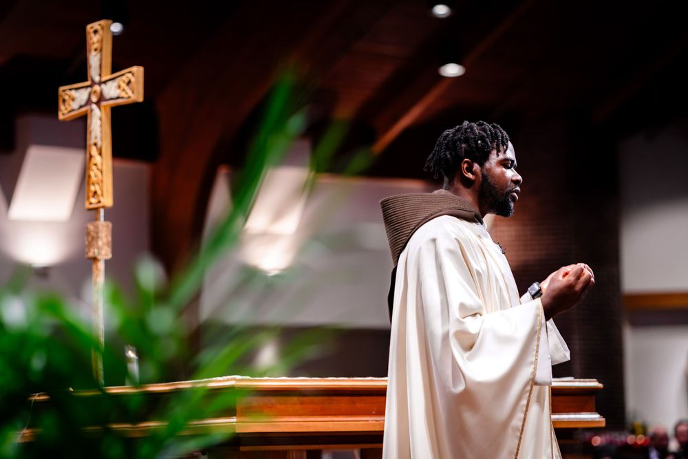 Priest in white robes conducts ceremony at church altar with wooden cross.
