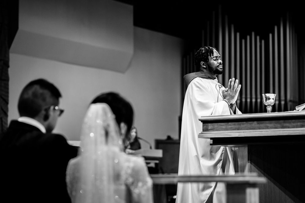 Black and white candid moments from a wedding ceremony in a church with dramatic lighting.
