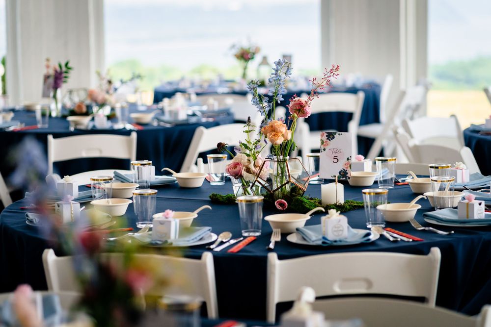 Wedding reception tables set with navy blue linens in a bright, window-filled venue.