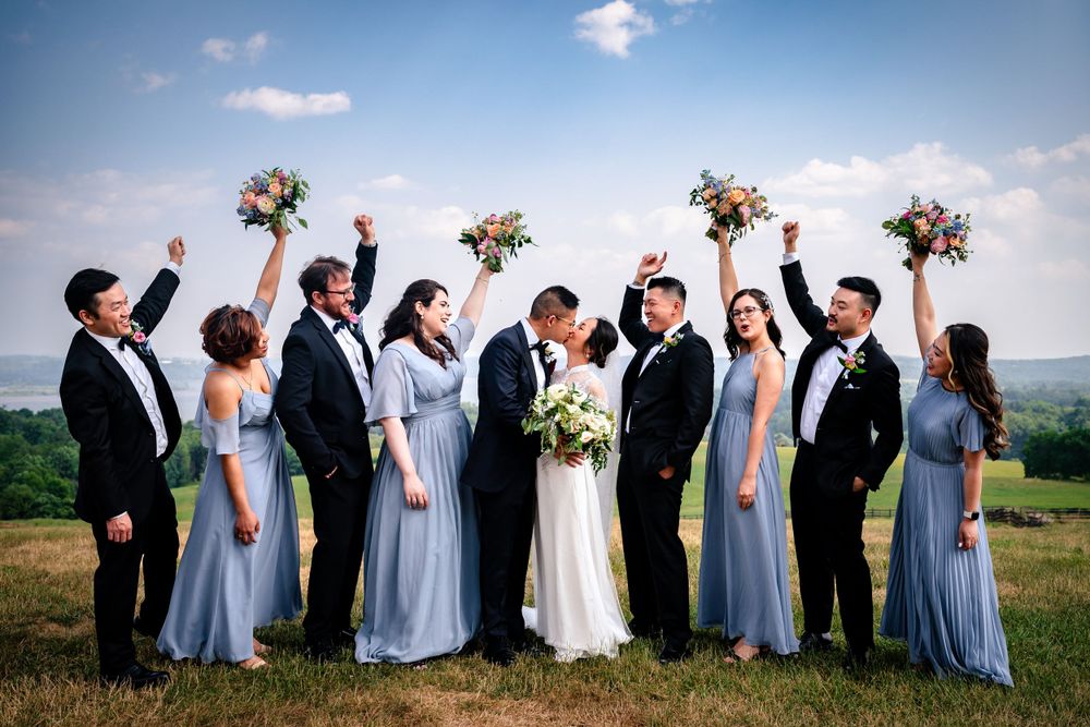 Wedding party in light blue dresses and black suits pose together against scenic mountain backdrop.
