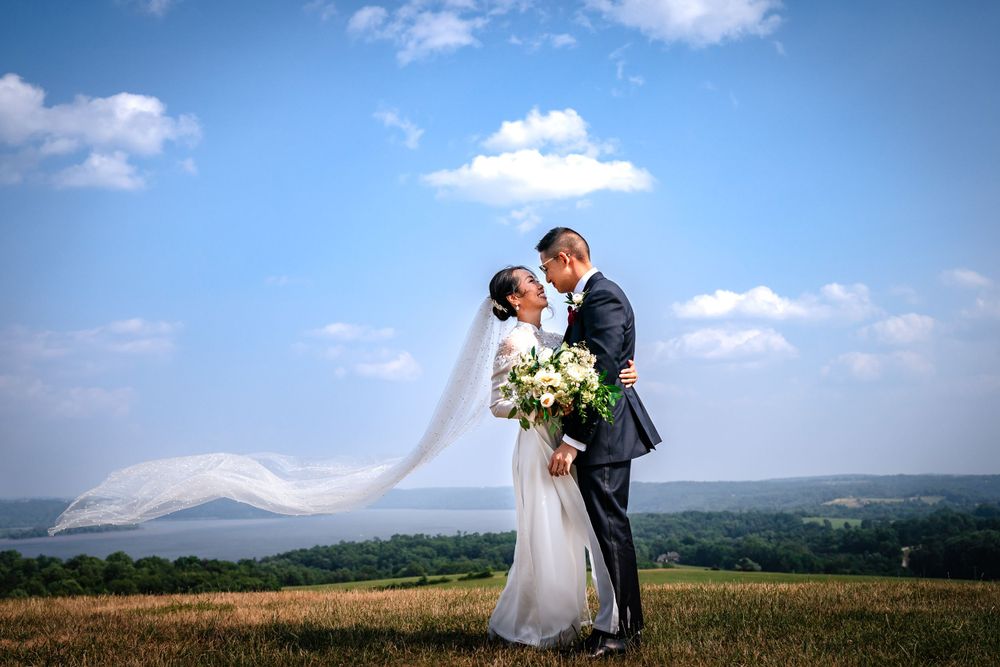 Wedding couple embraces on hilltop with dramatic mountain landscape in background.