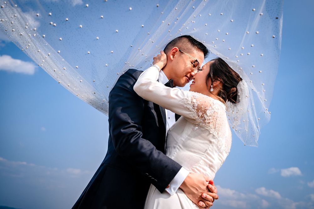 Wedding couple shares intimate moments under blue sky with flowing veil.