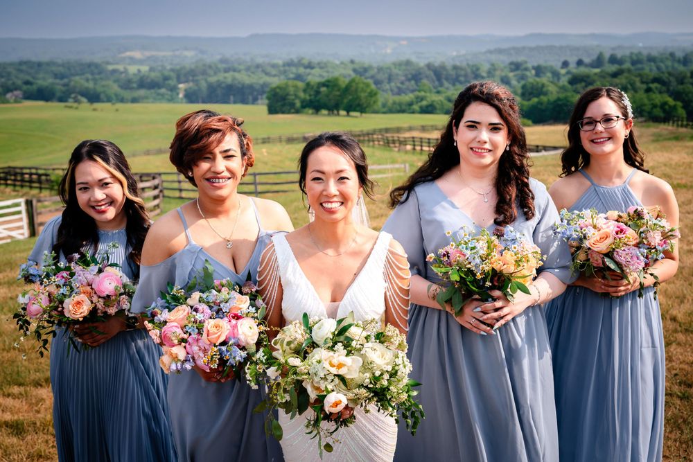 Bridesmaids in light blue dresses pose with bouquets against scenic landscape.