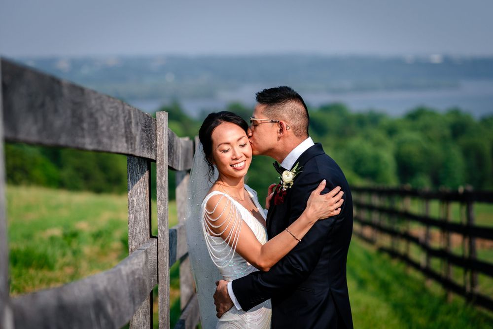 Wedding couple shares joyful moments along rustic wooden fence with countryside backdrop.
