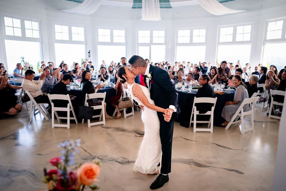 Panoramic view of an elegant white wedding reception venue with guests seated at round tables.