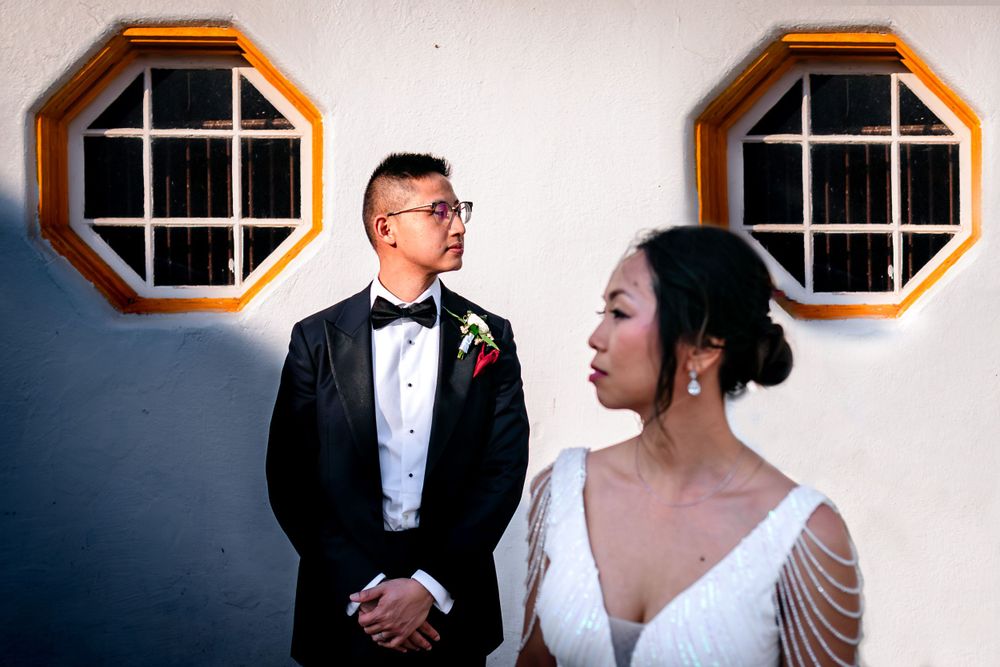 Elegant wedding couple posing by decorative octagonal windows in formal attire.