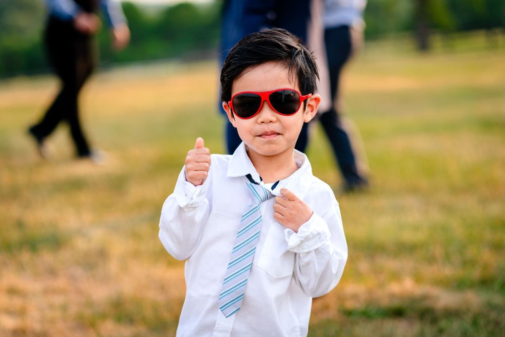 Young ring bearer in formal attire playing on grassy field during wedding.