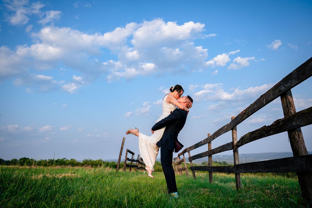 Wedding couple sharing romantic moments along a rustic wooden fence under blue skies.