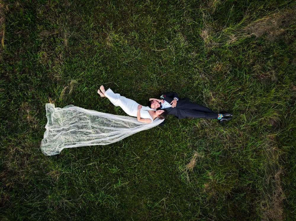 A flowing white wedding dress trails across lush green grass during an outdoor photoshoot.