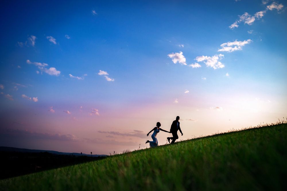 Silhouettes of figures stand on a grassy hill against a dramatic sunset sky with scattered clouds.