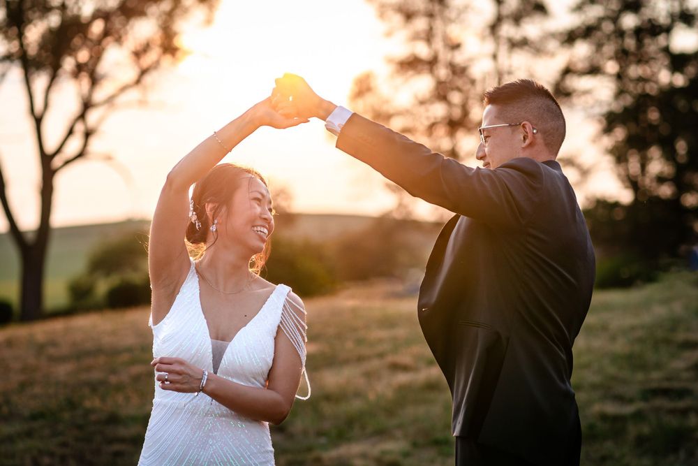 A couple shares a joyful moment during sunset in formal attire on a hilltop.