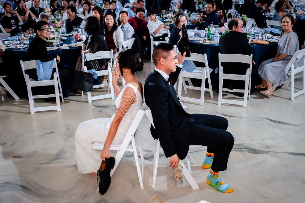 Wedding guests dance and celebrate at an indoor reception with white chairs and tables.
