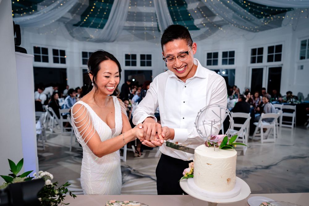 A couple cuts their wedding cake at a modern reception venue with white decor.