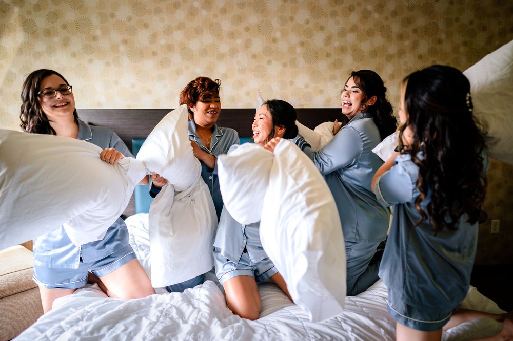 Group of people in white clothing sitting together on a bed sharing laughter.