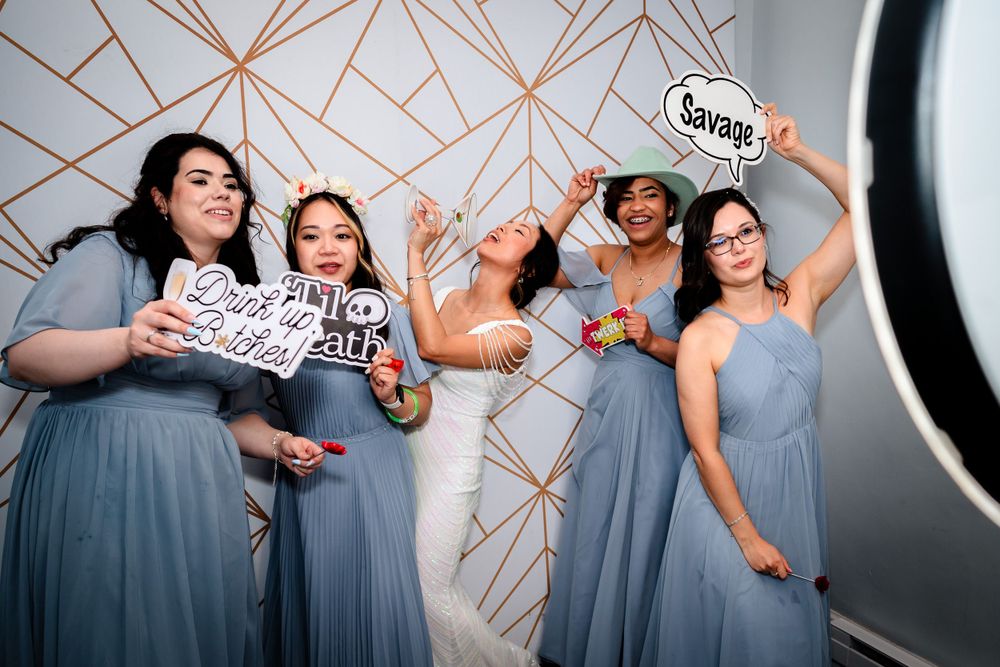 Bridesmaids in blue dresses posing against geometric rose gold wall backdrop at wedding.