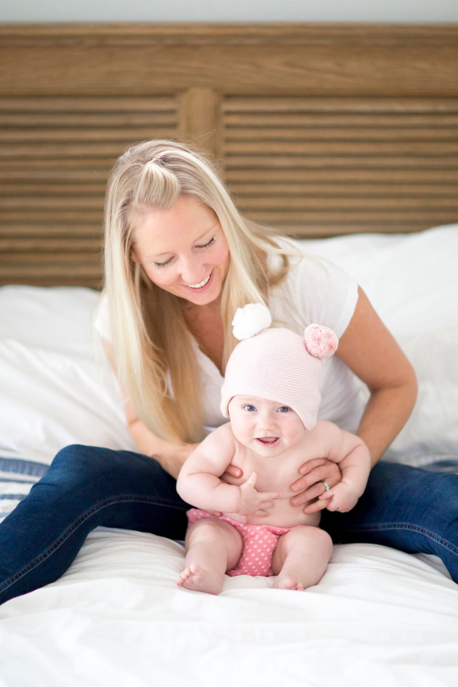 Parent and baby in pink hat share sweet moment on white bedding.