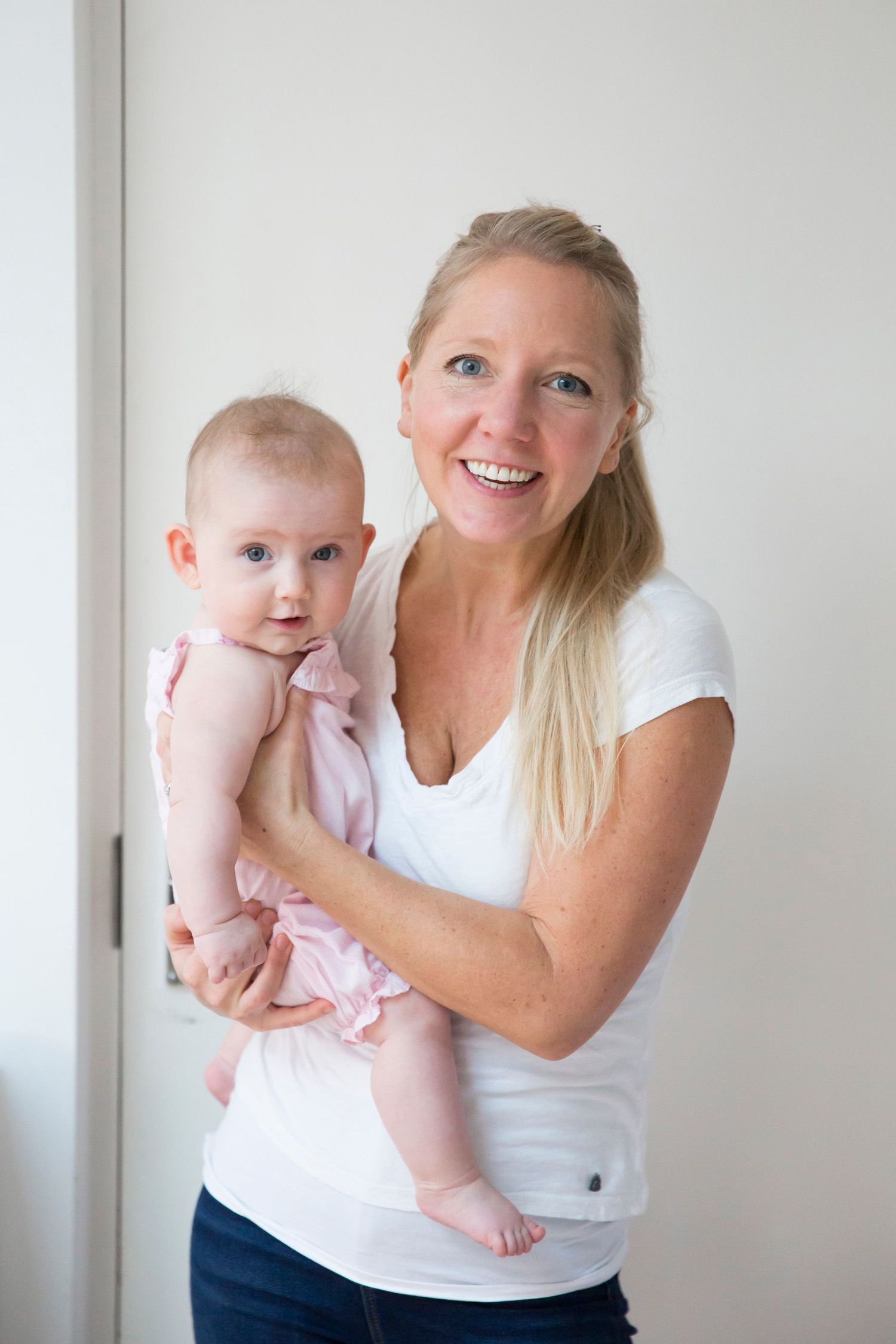 Parent and baby share a joyful moment together against white wall background.