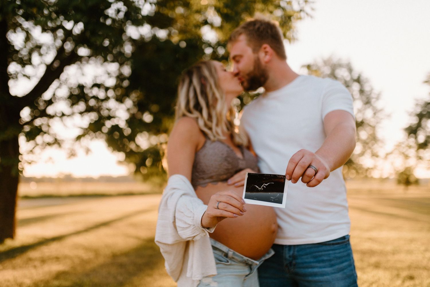 Couple shares intimate moment at sunset in open field.