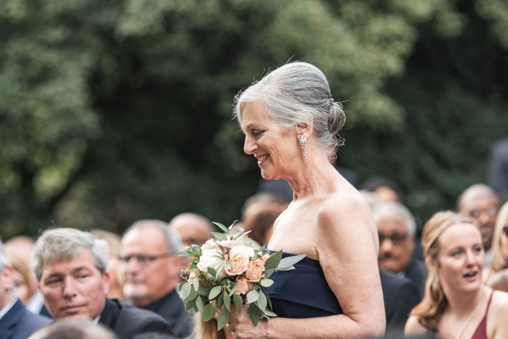 A wedding guest in a navy dress holding a peach-colored bouquet during an outdoor ceremony.