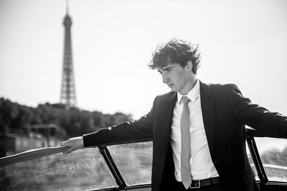 Black and white photo of someone in a suit posing with the Eiffel Tower in the background.