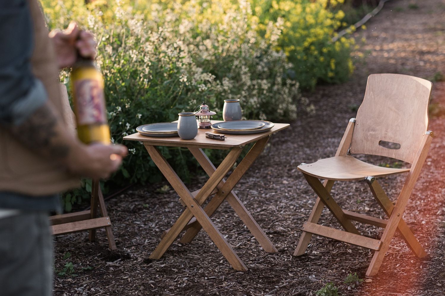 Wooden folding chairs and tables arranged outdoors in a natural setting.