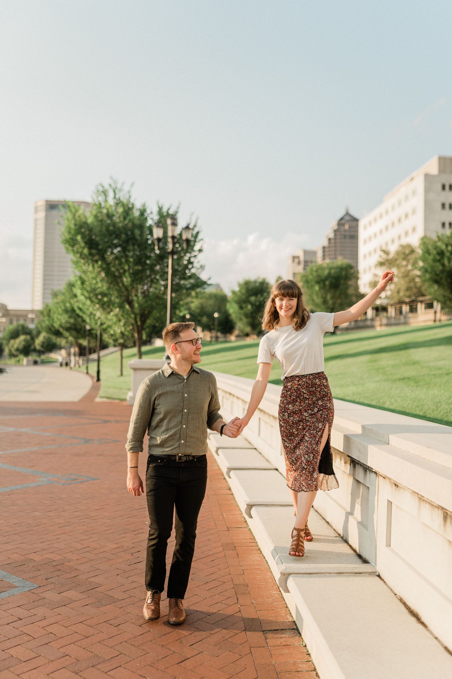 A couple strolls along a brick pathway with urban buildings in the background.