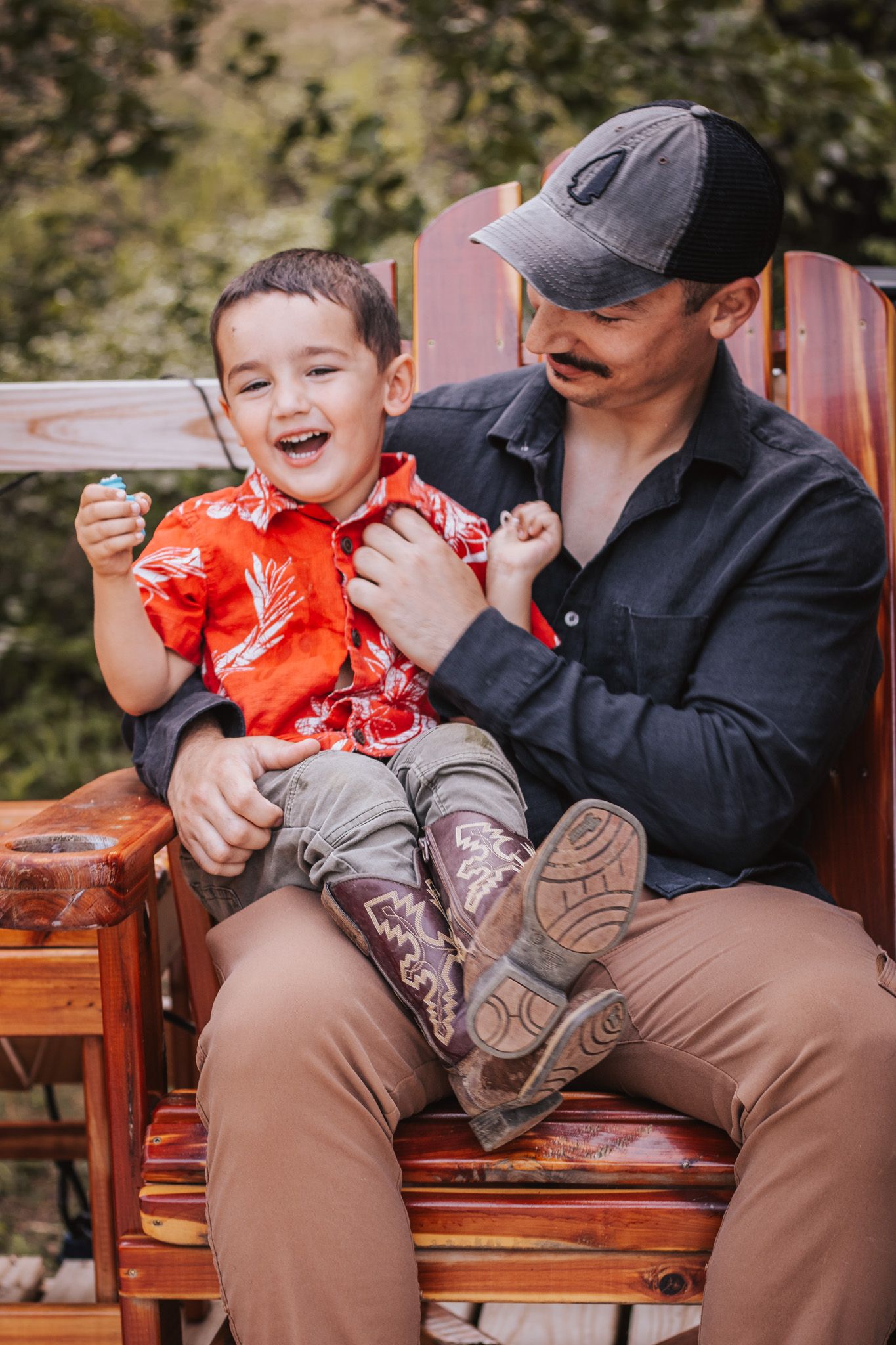 Father and child sharing laughs while sitting on wooden bench outdoors.