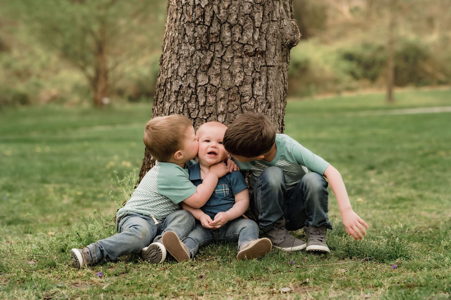 Three young children playing and laughing together under a large tree.