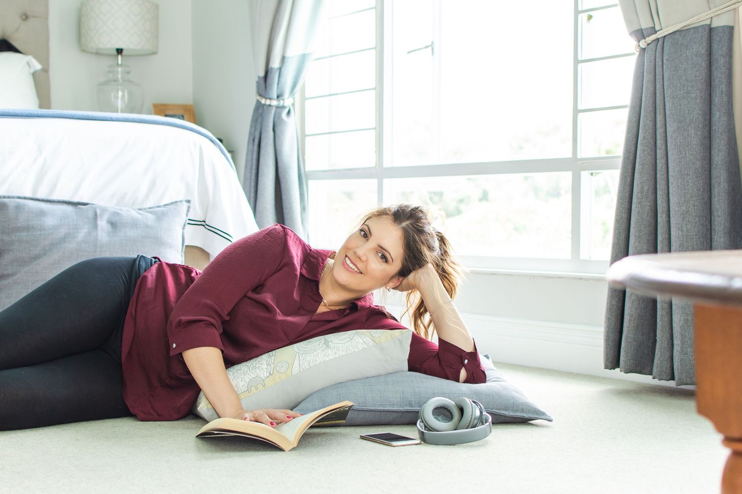 Person in burgundy sweater relaxing while reading a book on the floor.