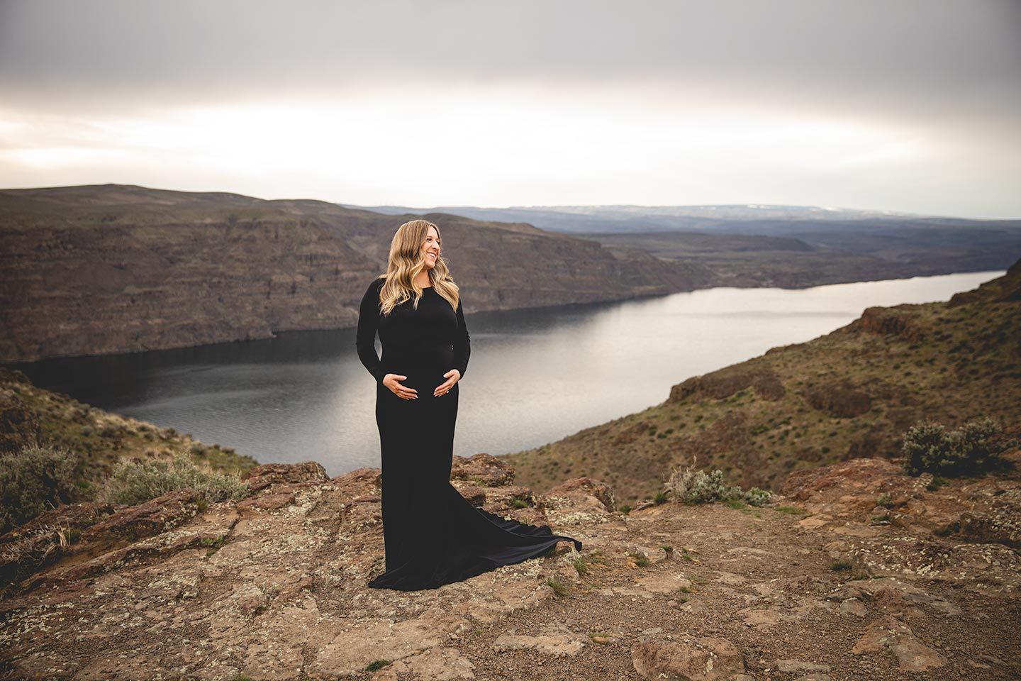 pregnant mother holding her arms around tummy with cliffs and the columbia river in the background.