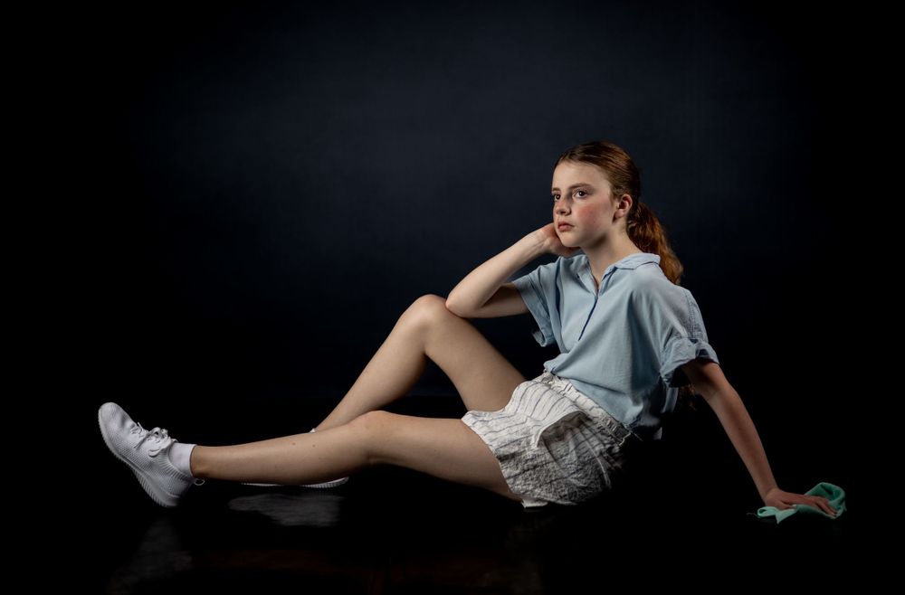 Casual studio pose in grey shirt and shorts lying against black background.