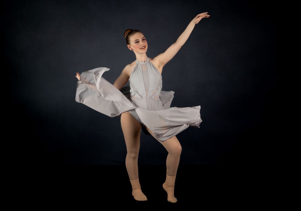 Dancer in flowing grey dress creates dramatic movement against dark background.