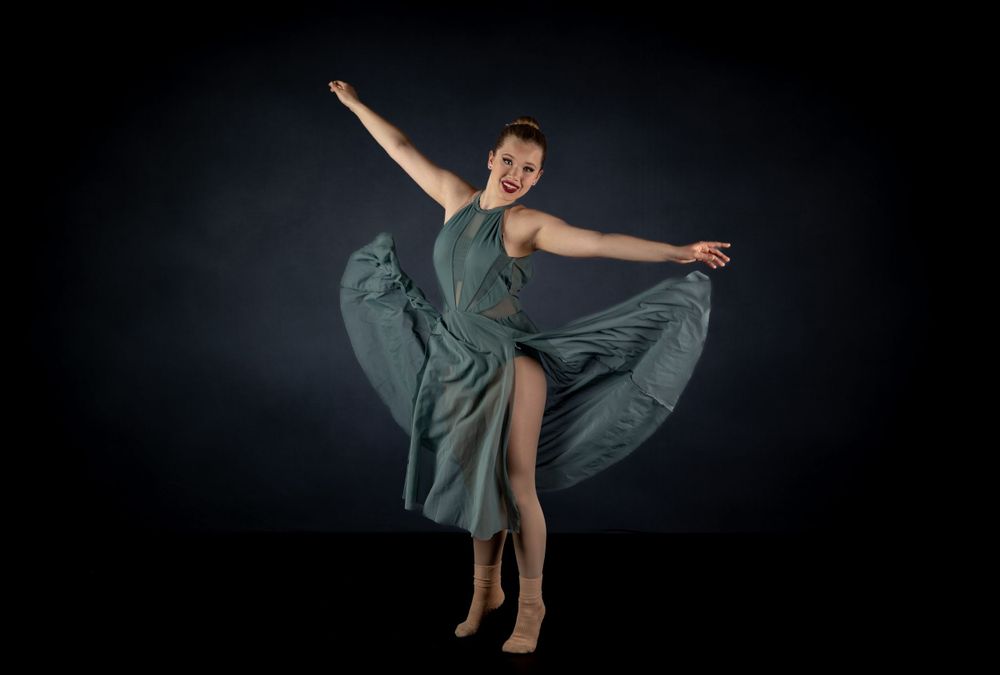 Dynamic dance pose with flowing teal dress creating dramatic movement against black backdrop.