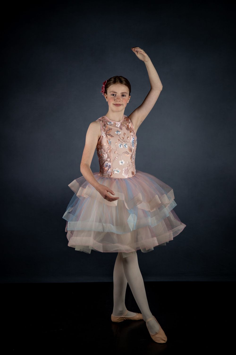 Ballet dancer in pale pink embellished tutu dress performs graceful pose.