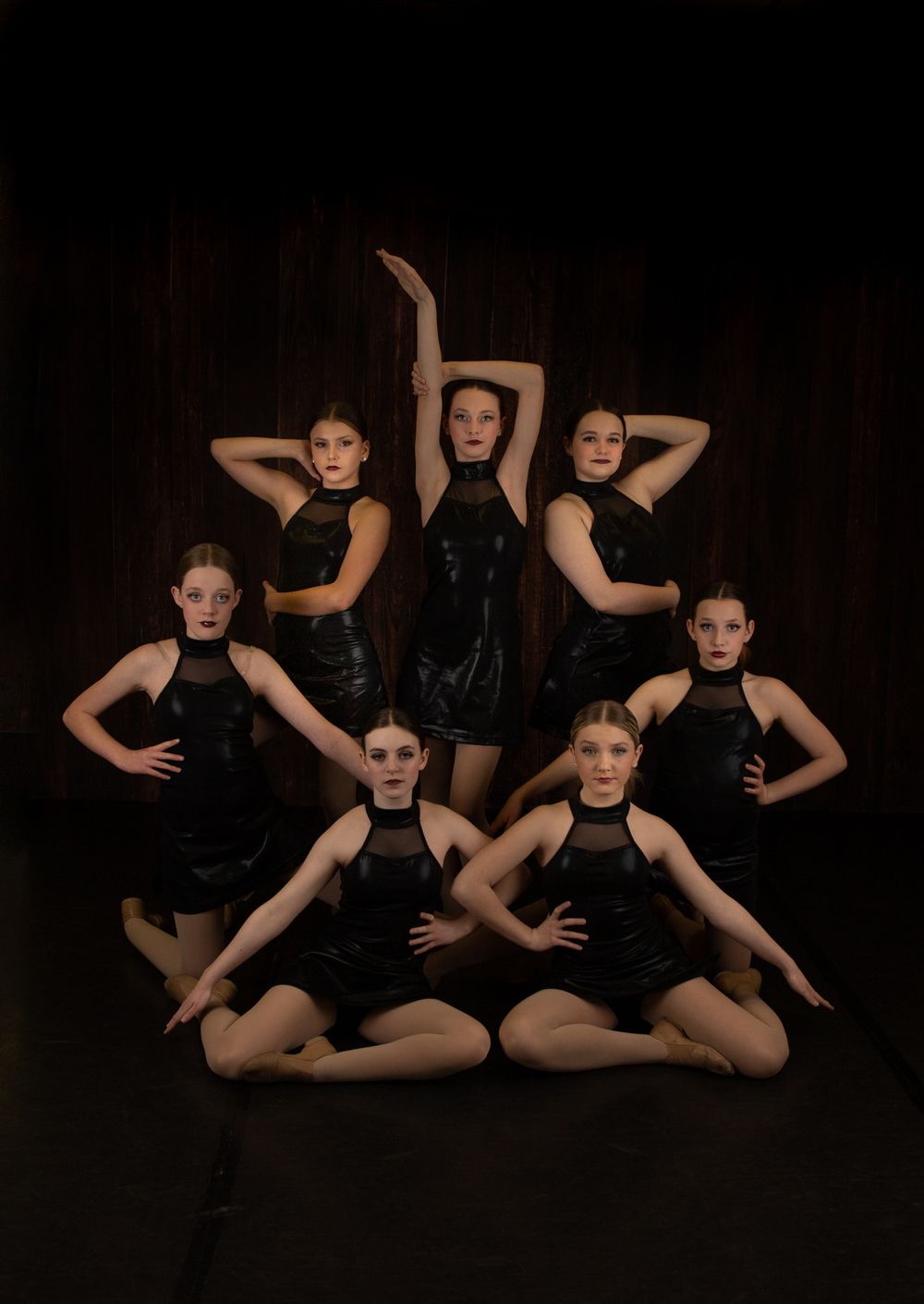Dance group in black costumes strikes dramatic pose in artistic formation.