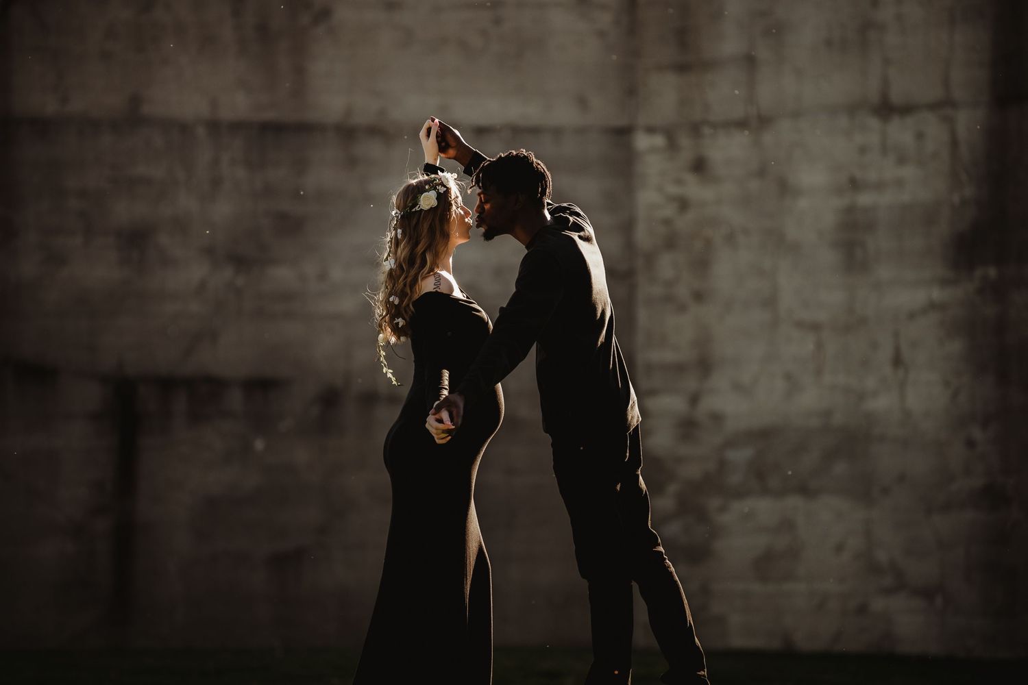 Dramatic silhouette of couple dancing in intimate pose against concrete wall.