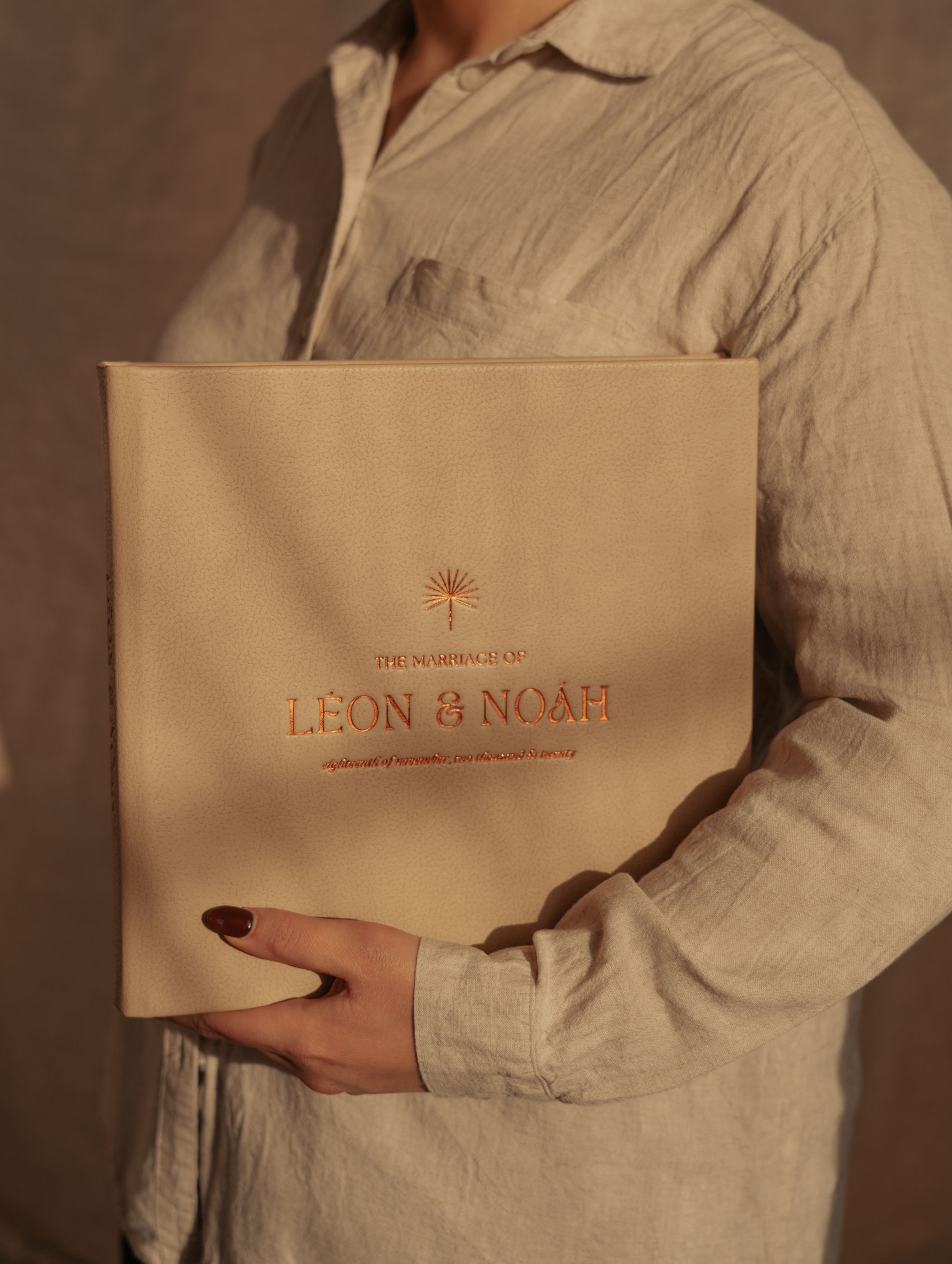 Hands holding a beige Leon and Noah branded package against a linen background.