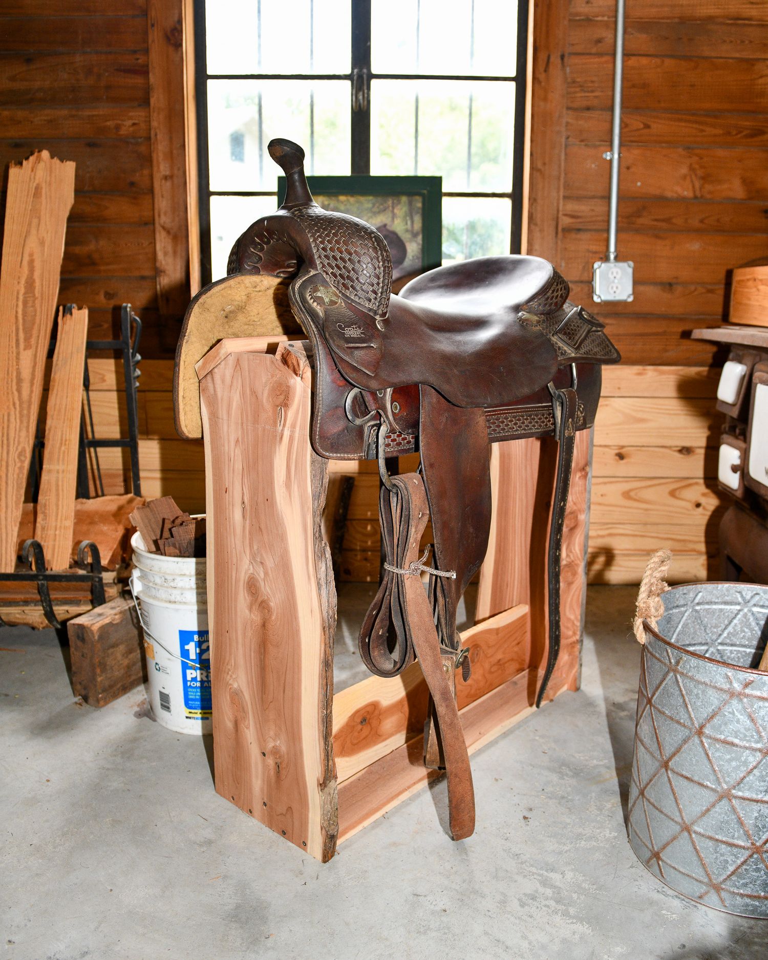 Western leather saddle displayed on a wooden stand in a rustic cabin interior.