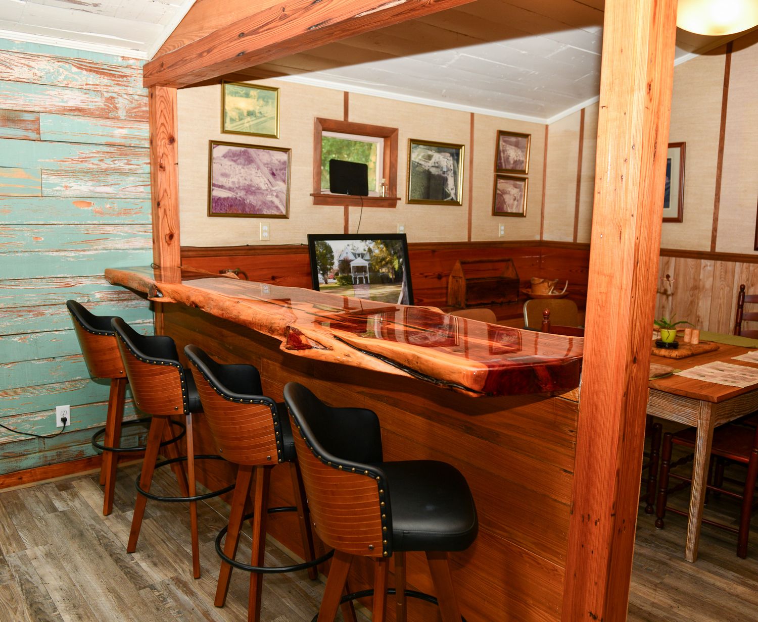 Rustic bar area with live edge wood counter and leather bar stools against turquoise wall.
