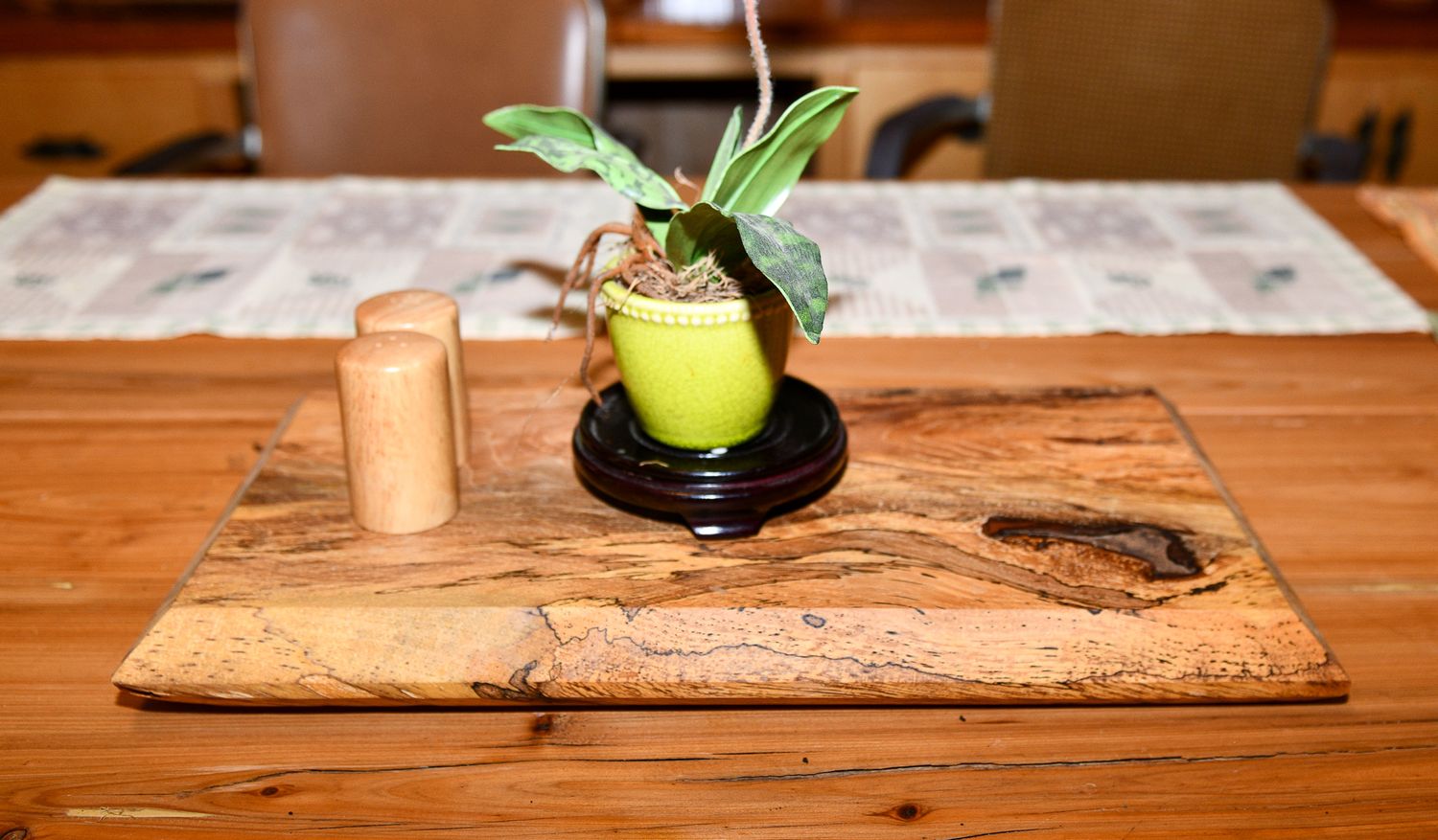 Decorative wooden serving board with potted plant and salt shaker on wooden table.