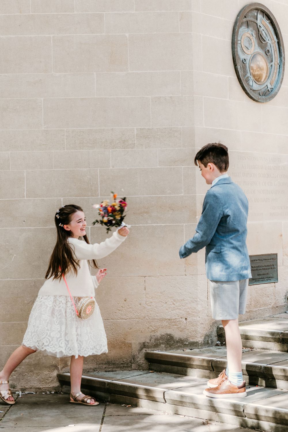 A sequence of playful photos showing two young children in white and blue outfits interacting by a wall.