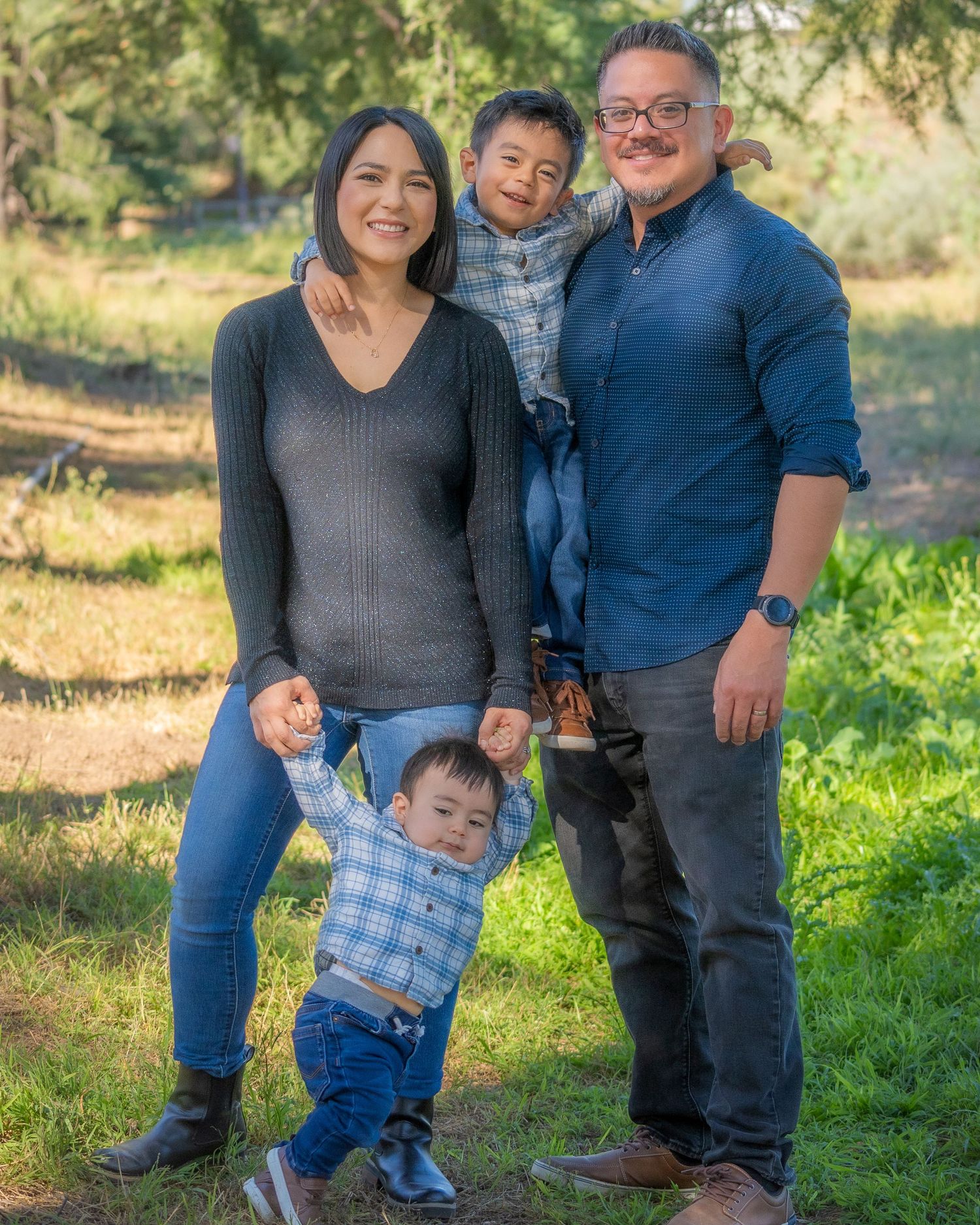 Happy family of four posing outdoors in a green park setting.