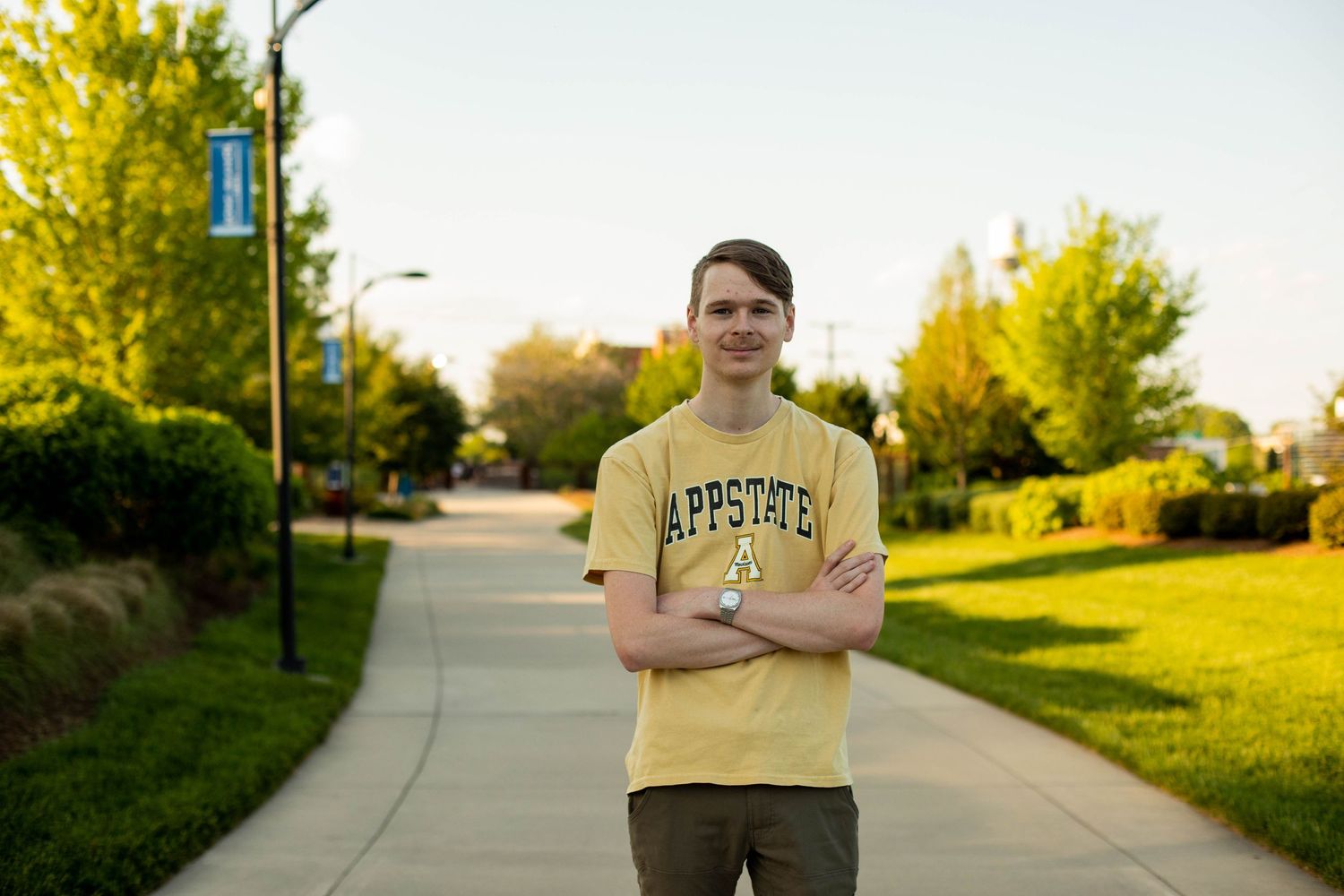 Student in yellow shirt poses outdoors during golden hour on campus pathway.