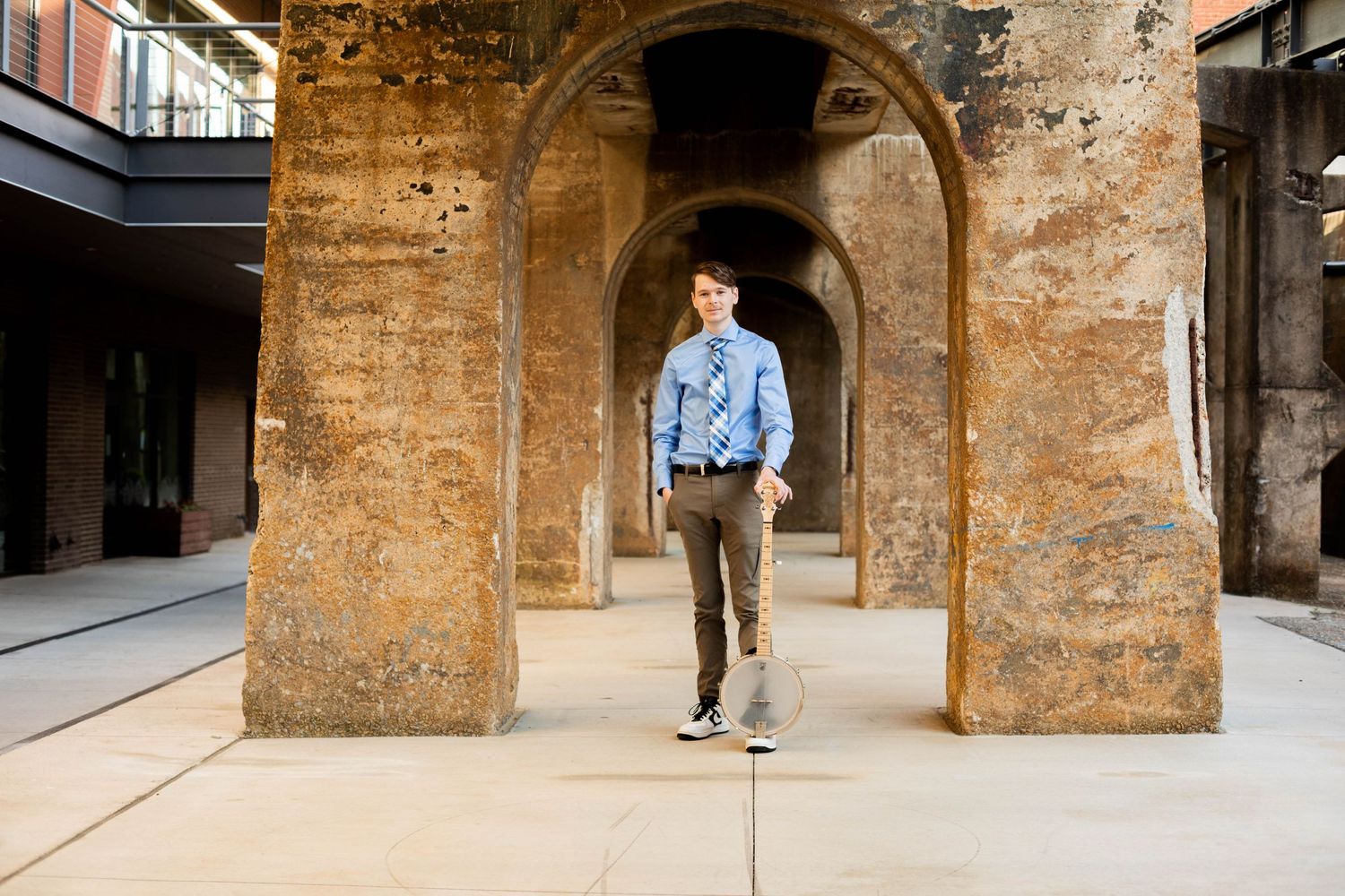 Graduate walks through historic stone archways in academic regalia.