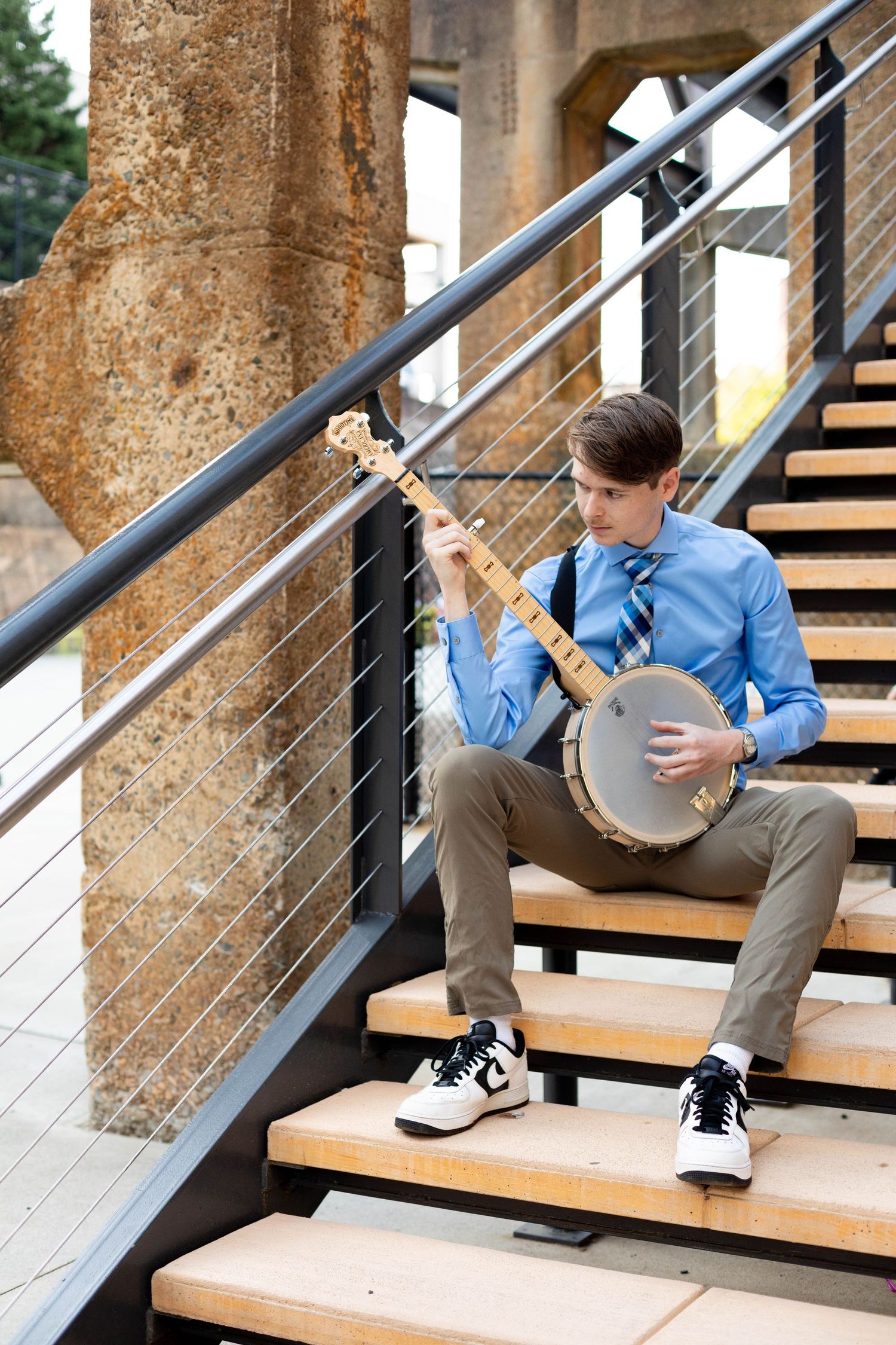 Graduate relaxes on industrial-style wooden stairs with metal railings.