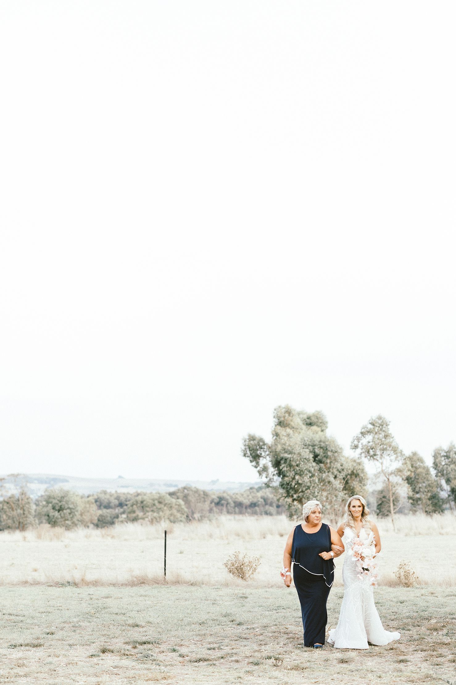 Two people walking across an open field at outdoor wedding venue.