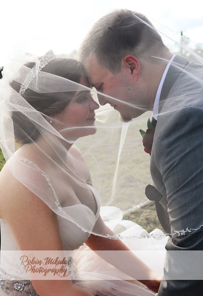 Bride and groom share intimate moments under a flowing white veil during their wedding ceremony.